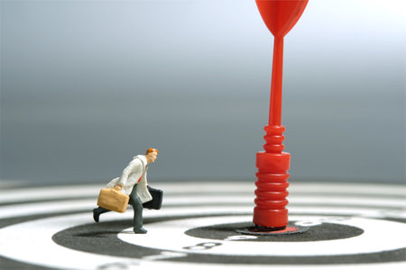 Miniature tiny people toy figure photography. A businessman running toward target arrow at the...
