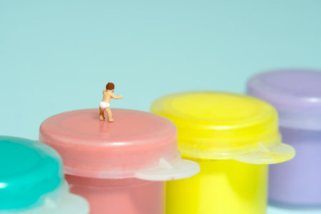 Miniature tiny people toy figure photography. Art study and learning concept. A boy toddler standing above paint tube. Isolated on blue background. Image photoの写真素材