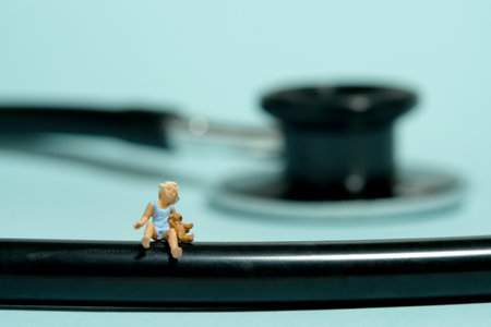 Miniature tiny people toy figure photography. A girl toddler sitting above stethoscope with teddy bear. Isolated on blue background. Image photoの写真素材
