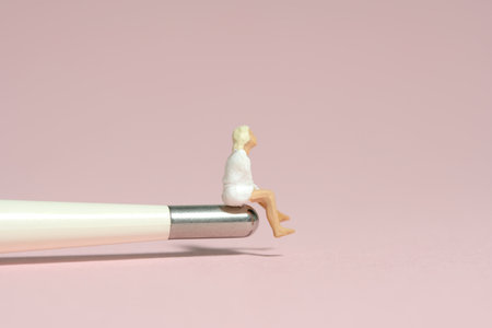 Miniature tiny people toy figure photography. A girl teenager sitting above iron tip on thermometer. Isolated on pink background. Image photoの写真素材