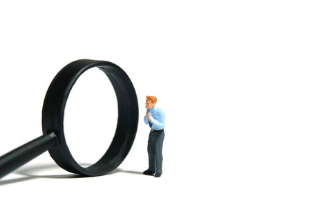 Miniature tiny people toy figure photography. A businessman getting ready, justify the tie beside magnifier glass. Isolated on white background. Image photoの写真素材