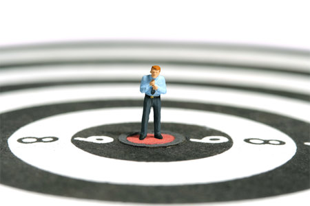 Miniature tiny people toy figure photography. A businessman getting ready, justify the tie above dartboard. Image photoの写真素材