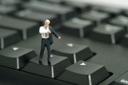Miniature tiny people toy figure photography. A businessman getting ready wearing suit standing above keyboard. Isolated on white background. Image photoの写真素材