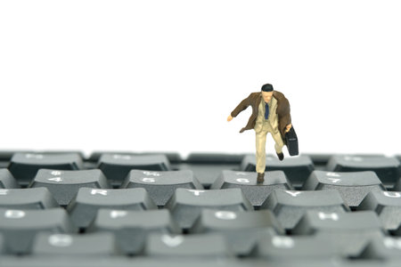 Miniature tiny people toy figure photography. A businessman running above black keyboard carrying briefcase. Isolated on white background. Image photoの写真素材