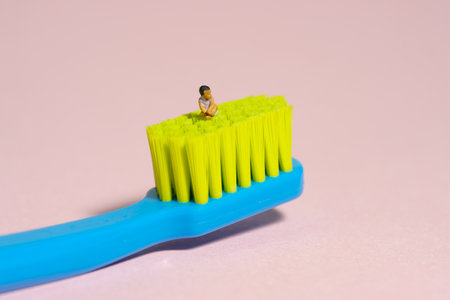 Miniature tiny people toy figure photography. A girl toddler baby seat above toothbrush. Isolated on pink background. Image photoの写真素材
