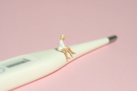 Miniature tiny people toy figure photography. A girl teenager sitting above thermometer. Isolated on...