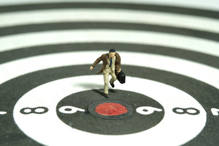 Miniature tiny people toy figure photography. A businessman running on dartboard carrying briefcase suitcase. Isolated on white background. Image photoの写真素材