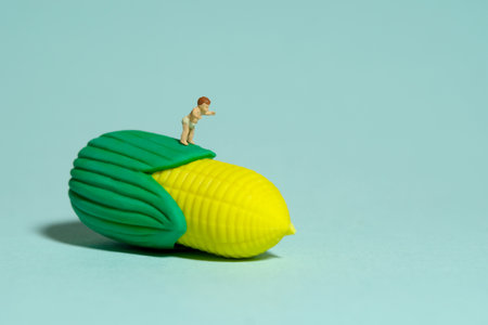 Miniature tiny people toy figure photography. Healthy food. A boy toddler infant feels happy looking at corn. Isolated on blue background. Image photoの写真素材