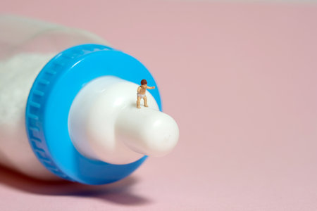 Miniature tiny people toy figure photography. A boy toddler infant whimpering, walking above milk bottle pacifier. Isolated on pink background. Image photoの写真素材