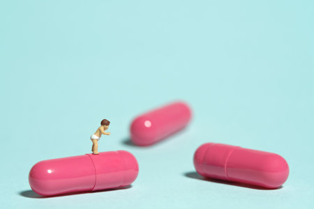 Miniature tiny people toy figure photography. A toddler baby walking above pink medicine pill tablet capsule. Isolated on blue background. Image photoの写真素材