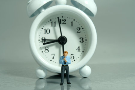 Miniature tiny people toy figure photography. A businessman getting ready, justify the tie in front of clock. Isolated on white background. Image photoの写真素材