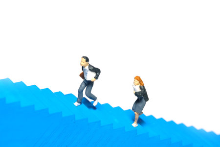 Miniature people toy figure photography. A boy and girl pupil student running on staircase. Isolated on a white background. Image photoの写真素材