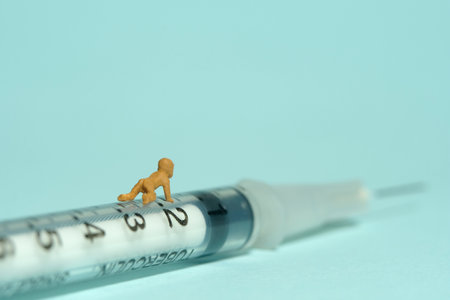 Miniature tiny people toy figure photography. An infant baby crawling above syringe. Isolated on blue background. Image photoの写真素材