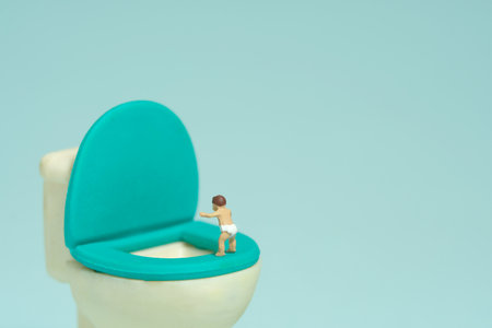 Miniature tiny people toy figure photography. A boy infant toddler standing above potty toilet closet. Isolated on blue background. Image photoの写真素材