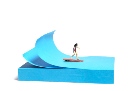 Creative miniature people toy figure photography. Sticky notes installation. A girl surfer riding big waves on surfing board. Isolated on white background. Image photoの写真素材