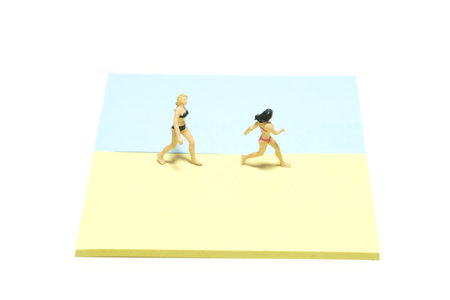Creative miniature people toy figure photography. Sticky notes installation. Two girls having fun running at the beach shore. Isolated on white background. Image photoの写真素材