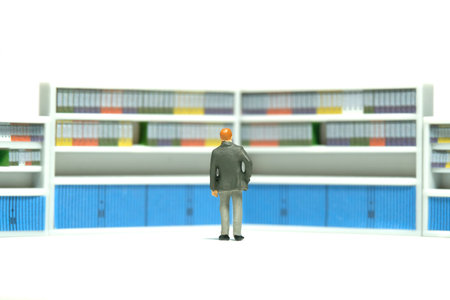 Miniature tiny people toy figure photography. Office file management. A businessman standing in front of archive document storage. Isolated on a white background. Image photoの写真素材