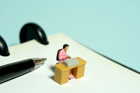 Miniature tiny people toy figure photography. minutes of meeting. A woman office worker seat on desk above notebook. Image photoの写真素材