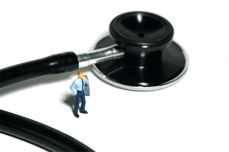 Miniature tiny people toy figure photography. A men standing in front of stethoscope, waiting for doctor health care check. Isolated on white background. Image photoの写真素材