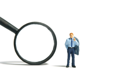 Miniature tiny people toy figure photography. A businessman standing beside black magnifier glass. Isolated on white background. Image photoの写真素材