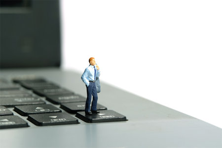 Miniature tiny people toy figure photography. Business concept illustration. A businessman standing above laptop notebook. Image photoの写真素材