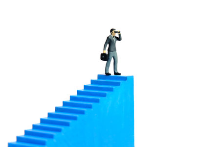 Miniature tiny people toys photography. Businessman using binocular telescope standing above blue stairway. Isolated on a white background. Image photoの写真素材