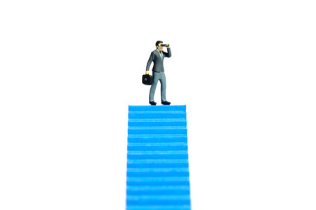Miniature tiny people toys photography. Businessman using binocular telescope standing above blue stairway. Isolated on a white background. Image photoの写真素材