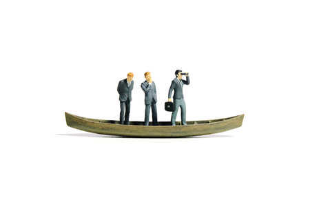 Miniature tiny people toy figure photography. Teamwork concept illustration. Businessman leader using binocular telescope sail with boat with team. Isolated on a white background. Image photoの写真素材