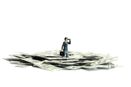 Miniature people toy figure photography concept illustration. Businessmen using binoculars buried on money cash paper pile. Isolated on a white background. Image photoの写真素材