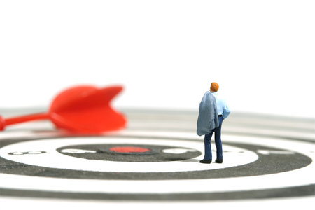 Miniature tiny people toy figure photography. Business concept illustration. A businessman standing above dartboard with red arrow, thinking strategy effectiveness. Image photoの写真素材