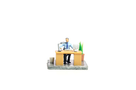 Miniature tiny people toy figure photography. Workspace station layout design concept. A businessmen seat on his desk, busy, working his job. Isolated on a white background. Image photoの写真素材