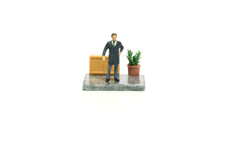 Miniature tiny people toy figure photography. Workspace station layout design concept. A businessman, ceo standing monitoring staff. Isolated on a white background. Image photoの写真素材