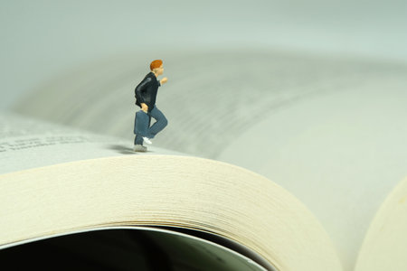 Miniature people toy figure photography. A boy pupil student running above opened book. Image photo