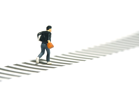 Miniature tiny people toy photography. Back side view of a boy pupil student running on zebra crossing crosswalk. Isolated on a white background. Image photoの写真素材