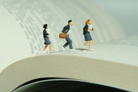 Miniature people toy figure photography. Three pupils, boy and girl student running above opened book. Image photoの写真素材