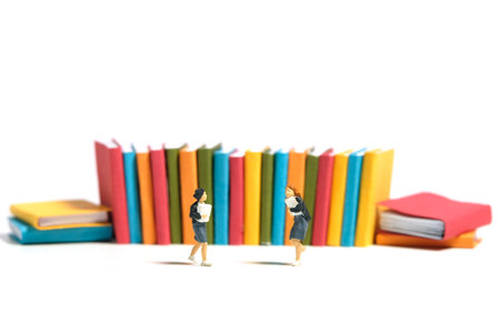 Miniature people toy figure photography. Two girl pupil students running in front of book row. Isolated on a white background. Image photoの写真素材