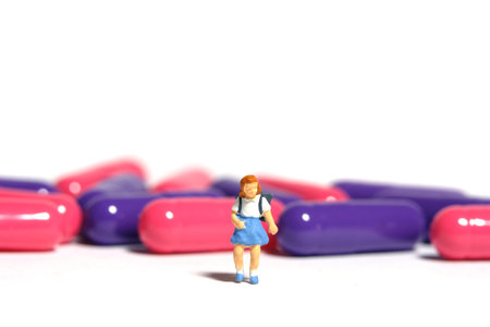 Miniature people toy figure photography. A girl student standing in front of medical drug pill. Isolated on white background. Image photoの写真素材
