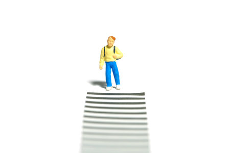 Miniature tiny people toy photography. A boy student waiting on sideroad zebra crossing. Isolated on white background. Image photoの写真素材