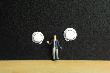 Miniature people toy figure photography. Business choice concept. A businessman standing on blackboard in between two blank bubble message. Isolated on blue background. Image photoの写真素材