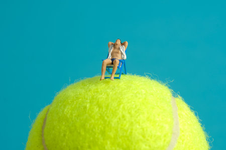 Miniature people toy figure photography. Travel destination concept, Men relaxing at beach chair above tennis ball, isolated on blue background. Image photoの写真素材