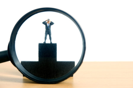 Businessmen standing using binoculars above black podium on desk with magnifier glass. Miniature tiny people toys photography. isolated on white background.の写真素材
