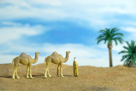 Miniature people toy figure photography. Middle eastern man wearing traditional clothes walking with camels in desert. Image photoの写真素材