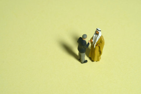 Miniature people toy figure photography. Partnership concept. Top view of Sultan and businessman make an handshake agreement. Isolated on yellow background. Image photoの写真素材