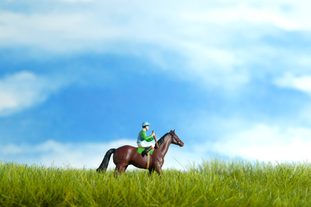 Miniature people toy figure photography. A jockey man riding horse at meadow field for training. Image photoの写真素材