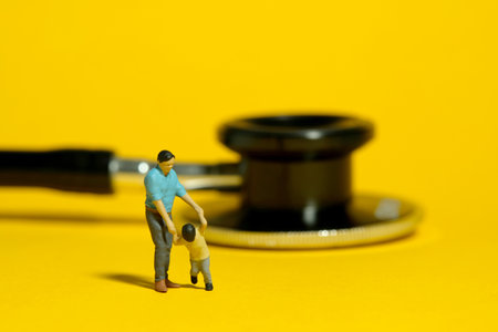 Miniature people toy figure photography. A father and son standing in front of stethoscope. Isolated yellow background. Image photoの写真素材