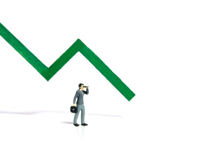 Miniature tiny people toy figure photography. Investment failure and loss concept. A businessman using binocular telescope standing in front of green bar declining graph. Image photoの写真素材
