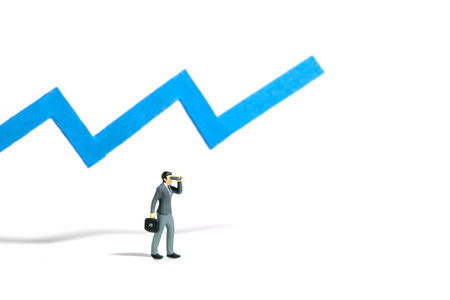 Miniature tiny people toy figure photography. Successful investment concept. A businessman using binocular telescope standing in front of blue bar increasing graph chart screen. Isolated on a whiteの写真素材