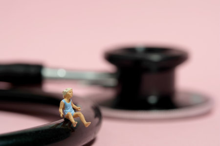 Miniature tiny people toy figure photography. A girl toddler sitting above stethoscope. Isolated on pink background. Image photoの写真素材
