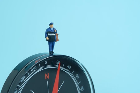 Miniature people toys conceptual photography. Address navigation. Postman courier with a compass, isolated on blue background.の写真素材