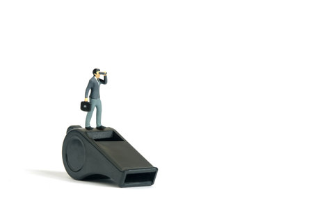 Miniature tiny people toys photography. Whistleblower concept illustration. Businessmen using binocular telescope standing above black whistle. Isolated on white background.の写真素材